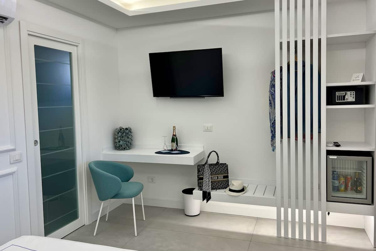 A modern living room with a flat-screen TV, a blue chair, a small table with a bottle and glasses, and a decorative item on the wall.