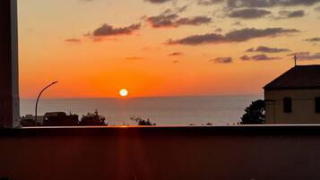 Ein Sonnenuntergangsblick vom Balkon mit Blick auf das Meer, mit einem Gebäude und einer Straßenlaterne im Vordergrund.