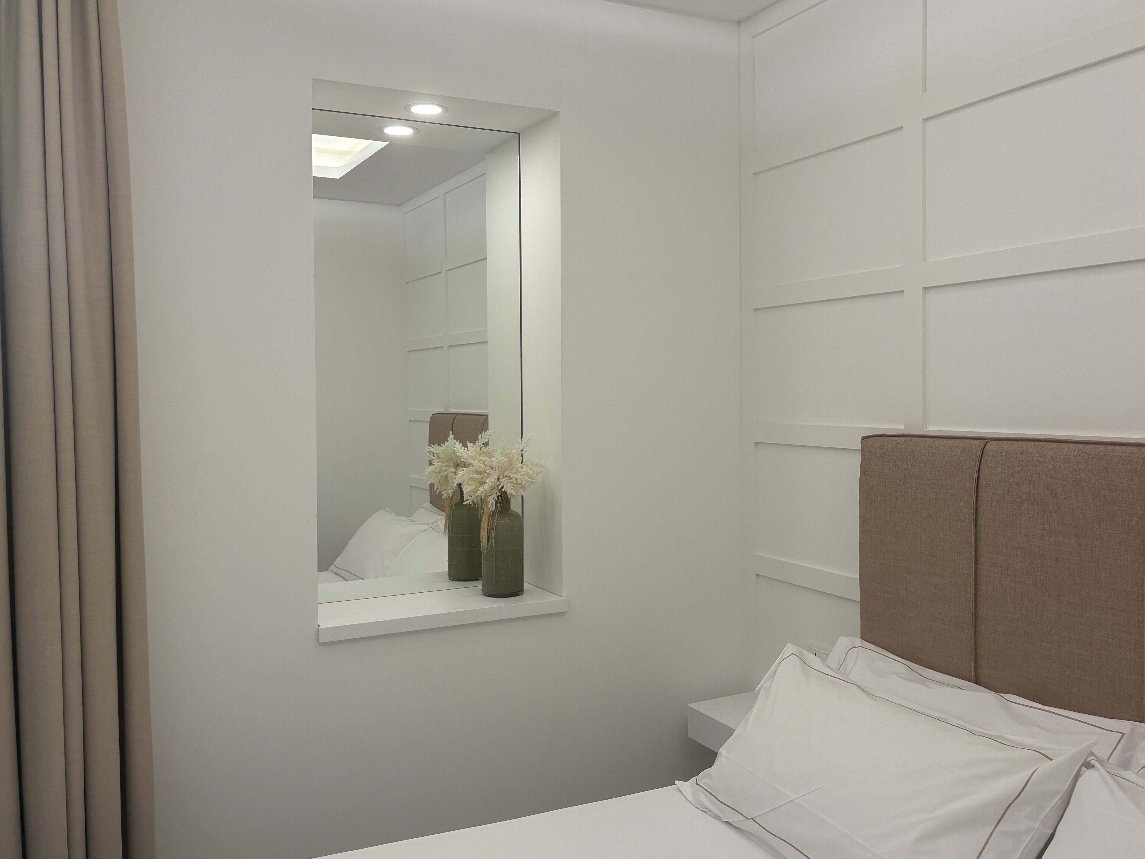Un dormitorio moderno con un espejo grande, una mesita de noche y un cabecero.