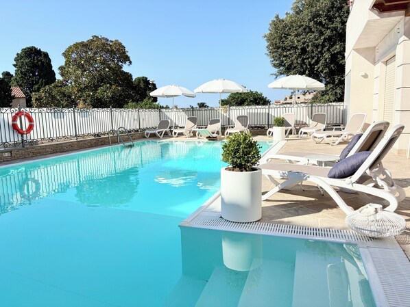 A swimming pool with lounge chairs and umbrellas, surrounded by a fence and trees. - Kairos Tropea (Tropea)