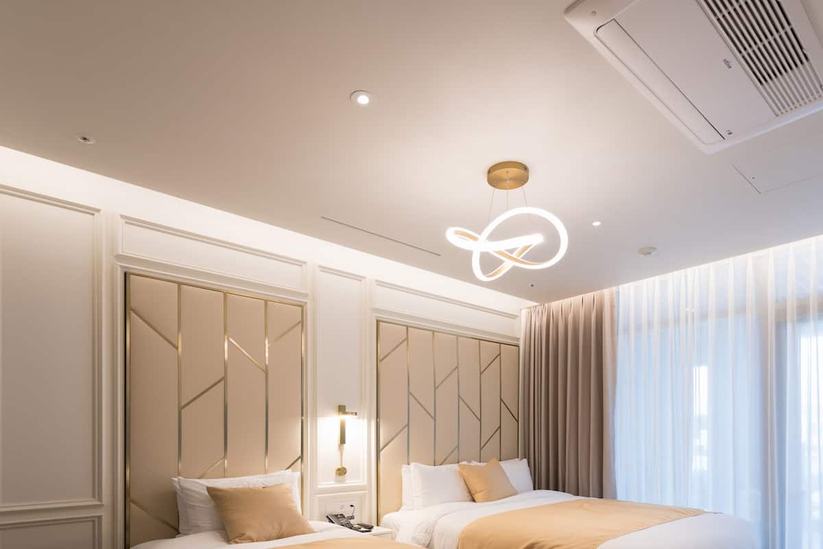 A modern hotel room with two beds, a large mirror, and a ceiling vent.
