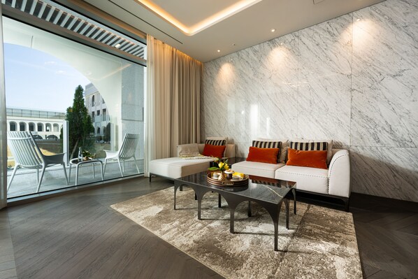 A modern living room with a glass wall, a white sofa with orange cushions, a coffee table, and a patterned rug. - The Siena Resort (Seogwipo)