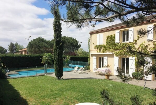A residential property with a swimming pool, a well-maintained lawn, and a two-story building with a balcony.