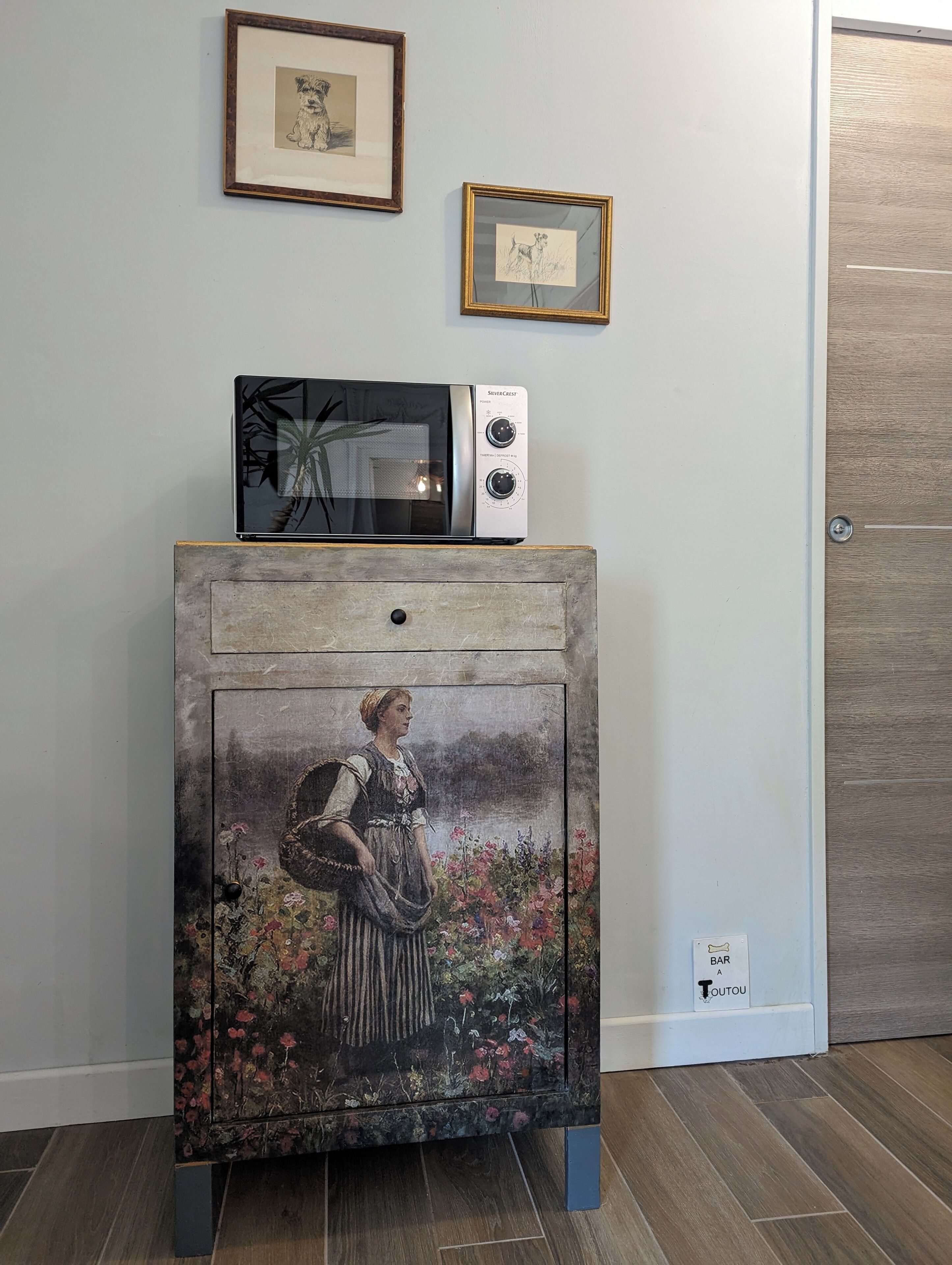Een kamer met een houten kast, een vintage schilderij, een magnetron en kunstwerken in een lijst aan de muur.