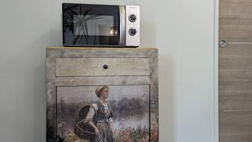 Een kamer met een houten kast, een vintage schilderij, een magnetron en kunstwerken in een lijst aan de muur.