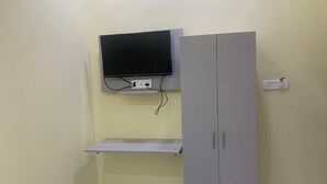 Una habitación con un televisor montado en la pared, un armario gris y un estante blanco.