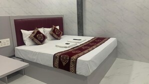 Una habitación de hotel moderna con suelo de mármol, cama con ropa blanca y una manta de oro y rojo, cabecero de mármol y mesita de noche.
