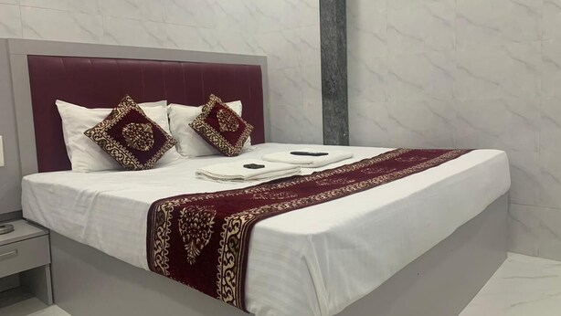 Una cama bien hecha con sábanas blancas, un plaid rojo y dorado, y almohadones decorativos.