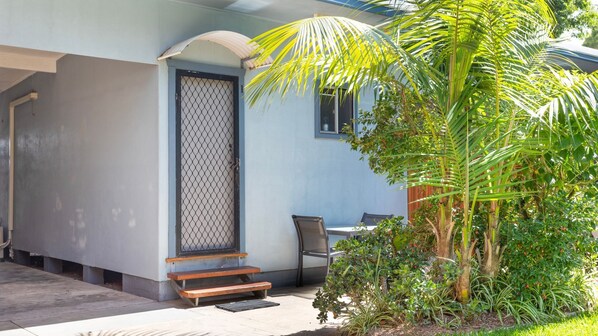 A building with a covered outdoor seating area, a door with a metal grill, and a palm tree.