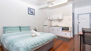 Een ruime, goed verlichte kamer met een bed, een kitchenette en een deur.