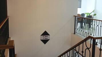 Una escalera con un cartel que indica los segundos y primeros pisos, una lámpara moderna y vistas a un balcón con sillas.
