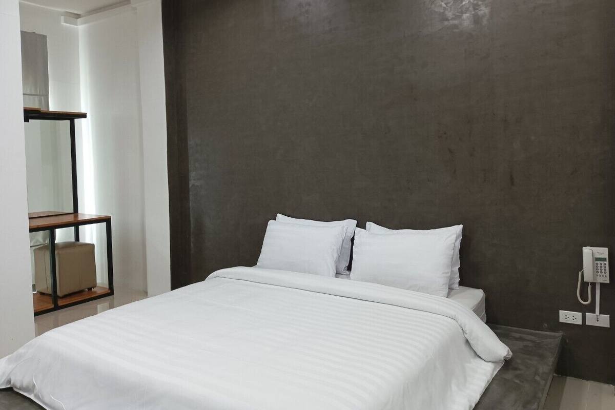 Quarto moderno com uma cama grande, um telefone ao lado da cama e uma pequena mesa com uma cadeira.