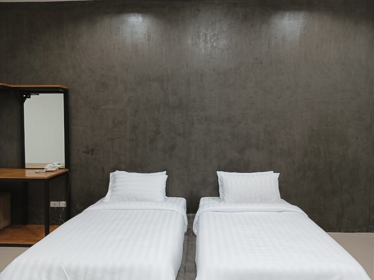 A room with two single beds, a wooden desk, and a mirror on the left wall.