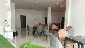 Un espace repas moderne avec un mélange de chaises grises et beiges disposées autour d’une table centrale, un réfrigérateur blanc et un four à micro-ondes posé sur un chariot.