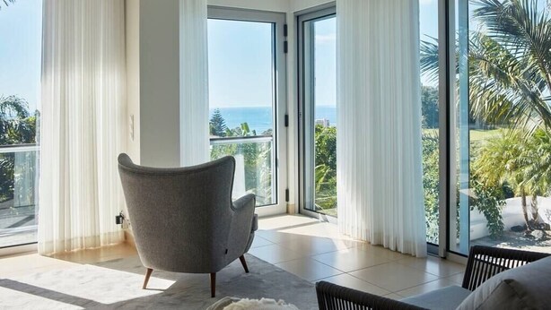 A spacious room with a large sliding glass door leading to a balcony with a view of the ocean.