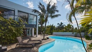 A modern house with a swimming pool, lounge chairs, and tropical plants.