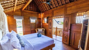 A wooden room with a bed, a wicker chair, and a balcony. - Villa Hana by Alfred in Bali (Seminyak)