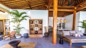 A spacious living area with a wooden ceiling, a sofa set, a dining table, and a large potted plant. - Villa Hana by Alfred in Bali (Seminyak)