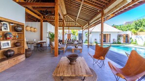 A covered outdoor area with a pool, wooden furniture, and a rustic table. - Villa Hana by Alfred in Bali (Seminyak)