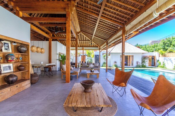 Un espacio al aire libre cubierto con piscina, muebles de madera y una mesa rústica.