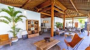A spacious indoor area with a wooden ceiling, a large potted plant, a wooden table, and a leather chair. - Villa Hana by Alfred in Bali (Seminyak)