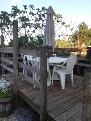 A wooden deck with a table and chairs, surrounded by a wooden fence and trees.