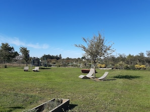 A grassy outdoor area with two lounge chairs, a tree, and a garden with various plants and flowers.