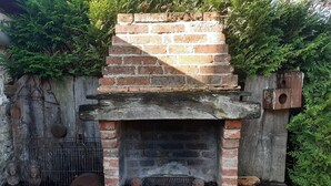 Una chimenea de ladrillo con una rejilla de metal, rodeada de follaje y un rústico muro de piedra.