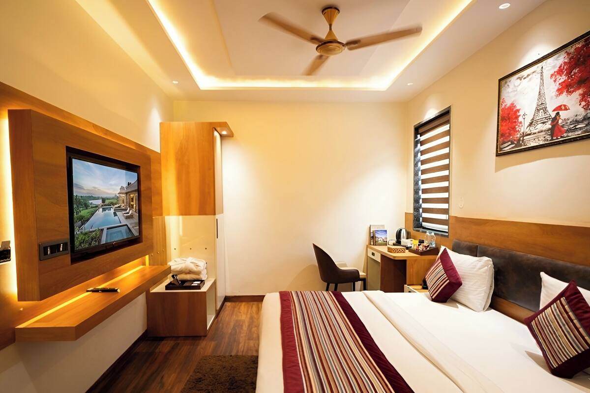 A hotel room with a bed, a desk, a chair, a TV, and a ceiling fan.