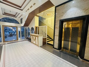 A spacious lobby with a marble floor, a staircase with a geometric design, and a large glass door. - Masaga by Qcent (Gurugram)