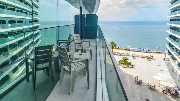 A balcony with a view of the sea, outdoor seating, and a glass railing. - GLOBALSTAY Batumi View Apartments. Beach (Batumi)