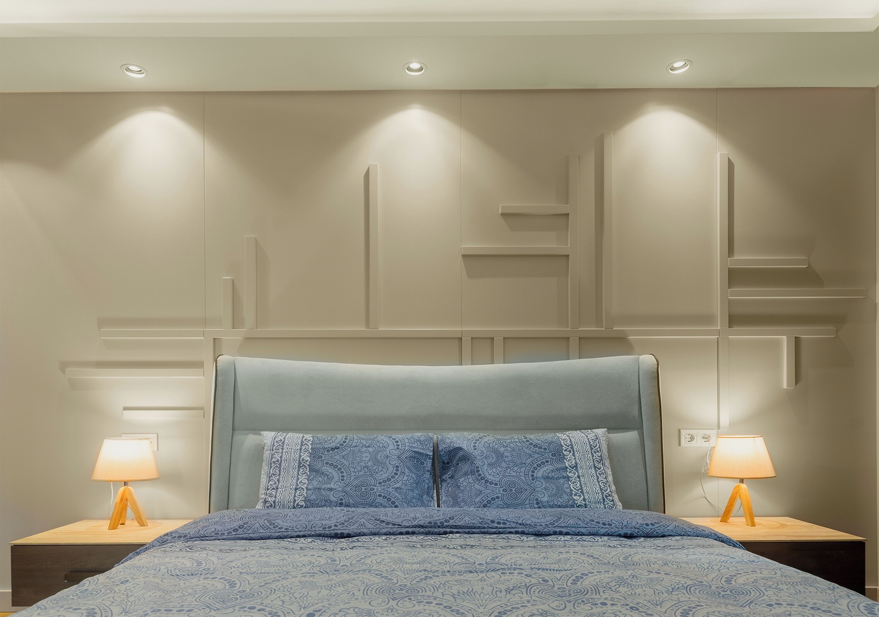 Un dormitorio con una cama, dos mesitas de noche con lámparas e iluminación empotrada en la pared.