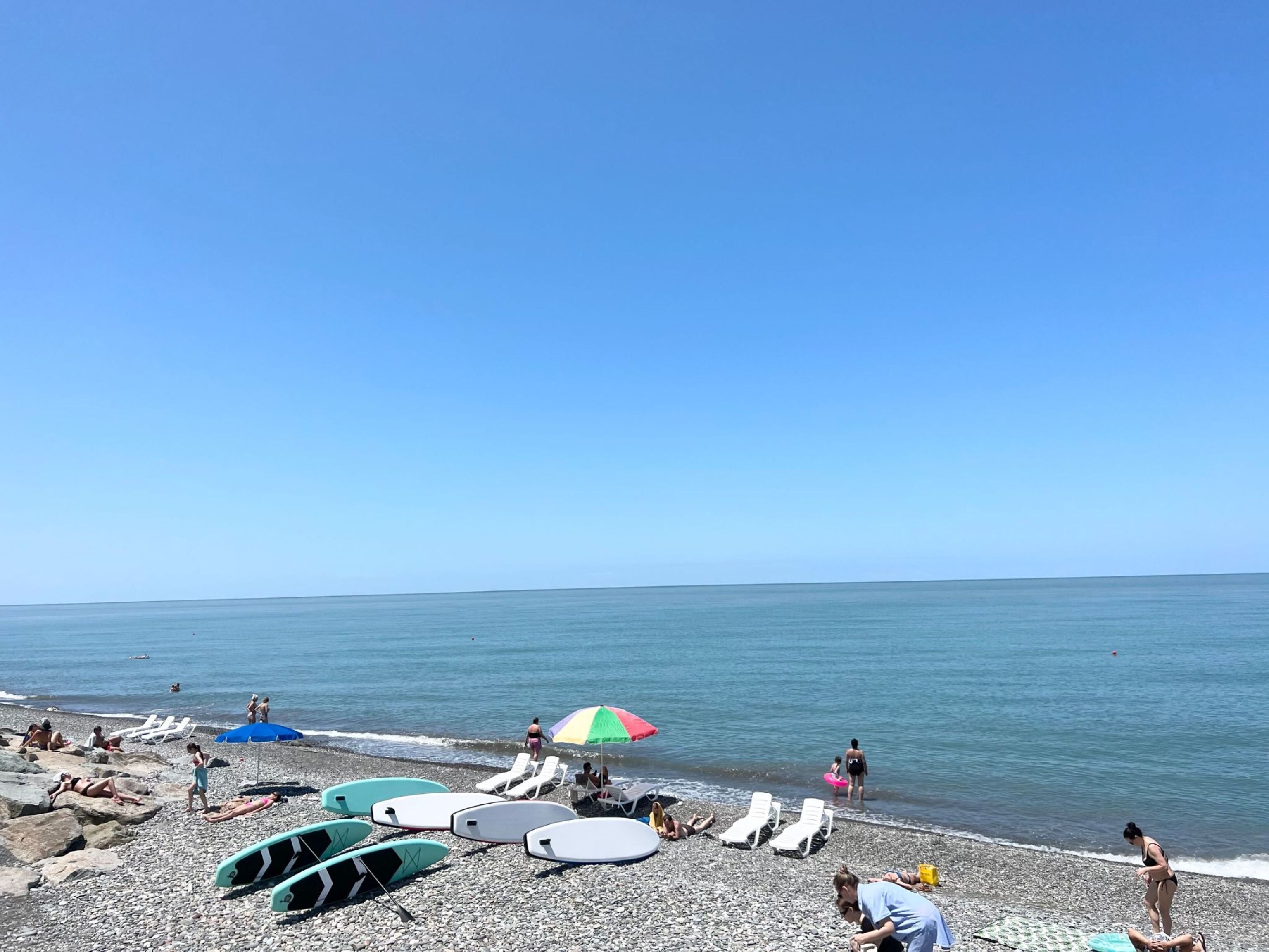 A pebbled beach with sun loungers, umbrellas, and surfboards.