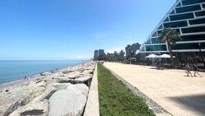 A coastal promenade with a modern building, a rocky shoreline, and a clear blue sky. - GLOBALSTAY Batumi View Apartments. Beach (Batumi)