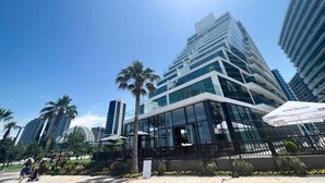 A modern building with a glass facade, surrounded by palm trees and other greenery. - GLOBALSTAY Batumi View Apartments. Beach (Batumi)