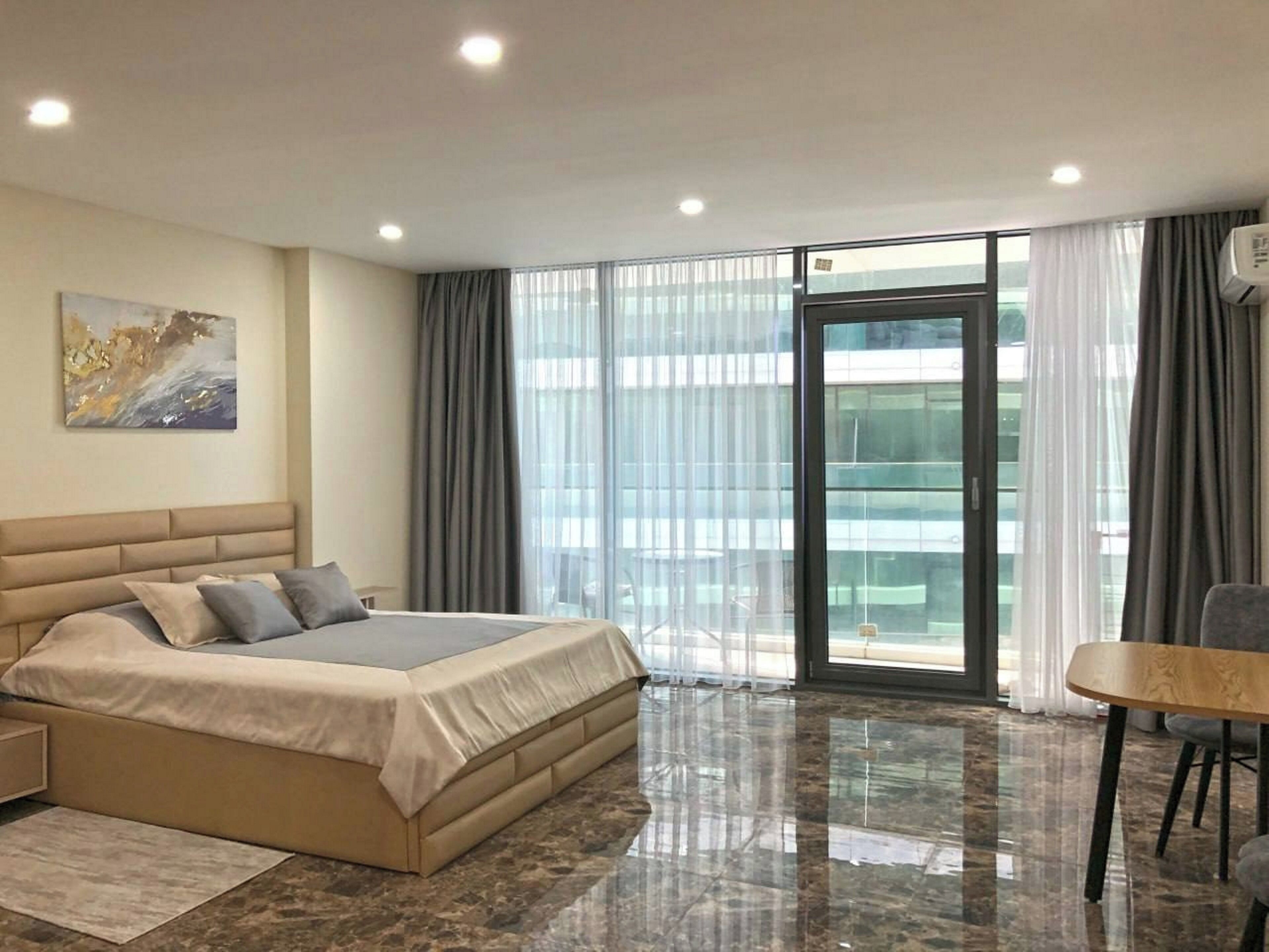Una habitación de hotel moderna con una cama grande, una mesa de comedor y vistas a la ciudad desde la ventana.