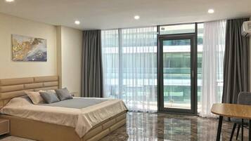 Una habitación de hotel moderna con una cama grande, una mesa de comedor y vistas a la ciudad desde la ventana.