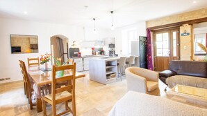 A modern living room with a dining area, a kitchen, and a large window. - Charming Country House in Tourtoirac, Pets Allowed (Tourtoirac)