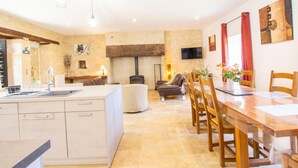 A spacious kitchen with a central island, a dining area with wooden chairs and a table, and a cozy seating area with a sofa and a fireplace. - Charming Country House in Tourtoirac, Pets Allowed (Tourtoirac)