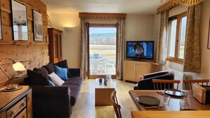A cozy living room with a sofa, TV, wooden cabinets, and a dining area with a table and chairs. - Apartment with view and parking - 6 guests (Samoëns)
