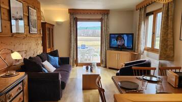A cozy living room with a sofa, TV, wooden cabinets, and a dining area with a table and chairs.