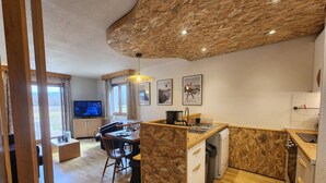 A modern kitchen with wooden accents, a dining area with a TV, and a view of the outdoors. - Apartment with view and parking - 6 guests (Samoëns)