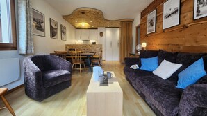 A cozy living room with a dark purple sofa, a wooden coffee table, and a dining area with a wooden table and chairs. - Apartment with view and parking - 6 guests (Samoëns)