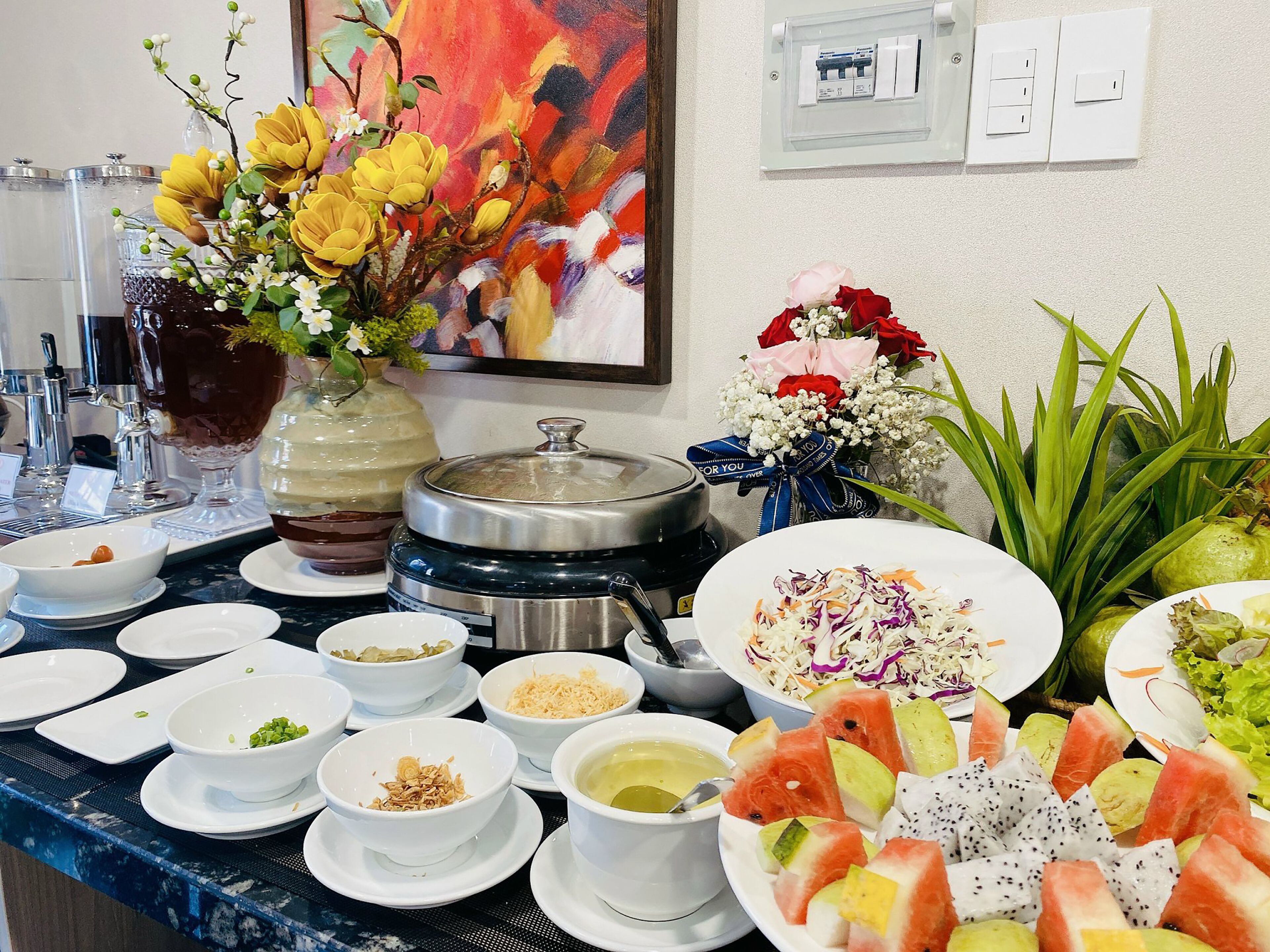 Een buffet met verschillende gerechten, een decoratieve vaas met bloemen en een schilderij aan de muur.