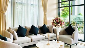A modern living room with a sectional sofa, two side tables, and large windows with curtains. - Hera Luxury Hotel (Ho Chi Minh City)