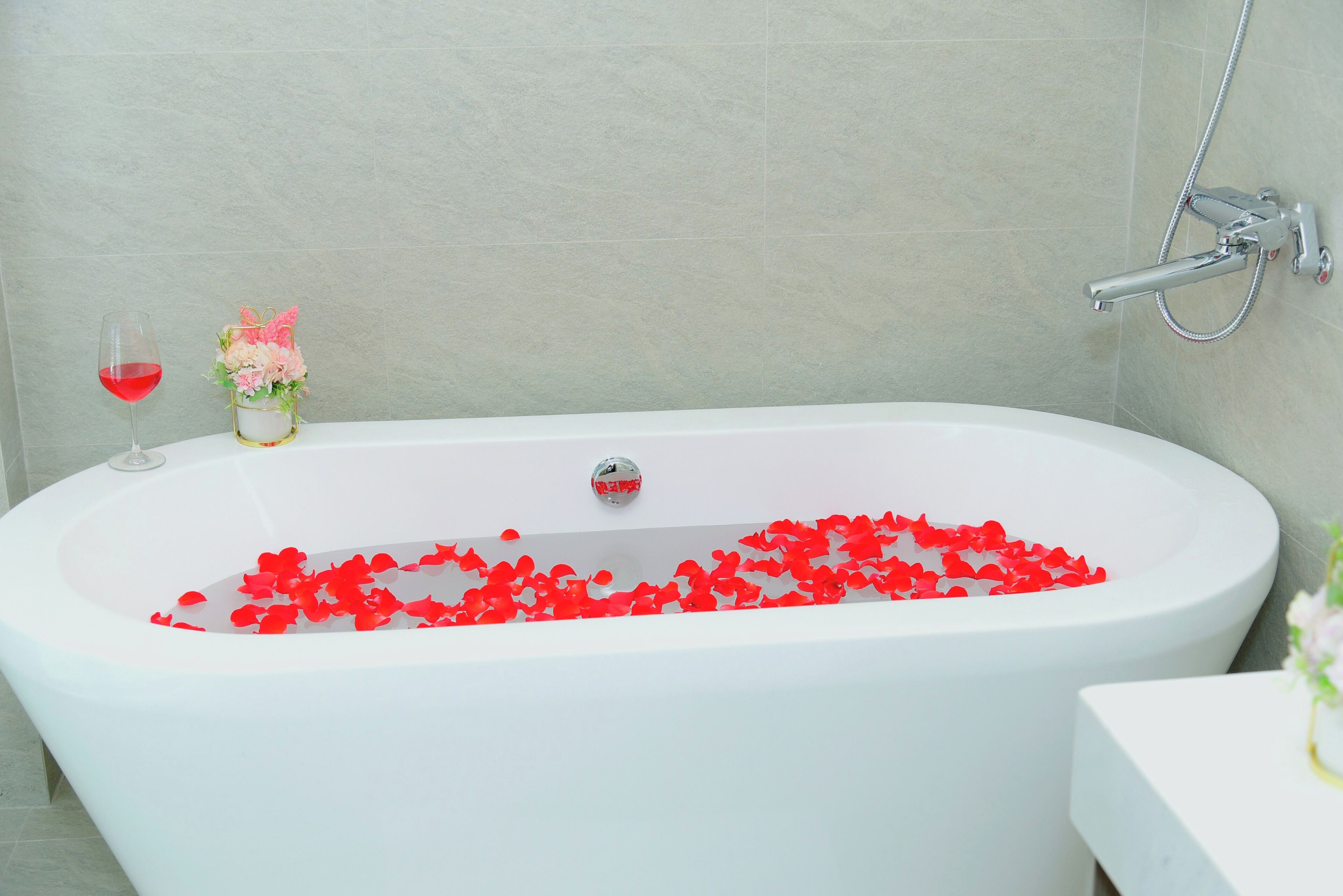 Une baignoire remplie de pétales de roses rouges, un verre de vin rouge et un vase avec des fleurs roses.