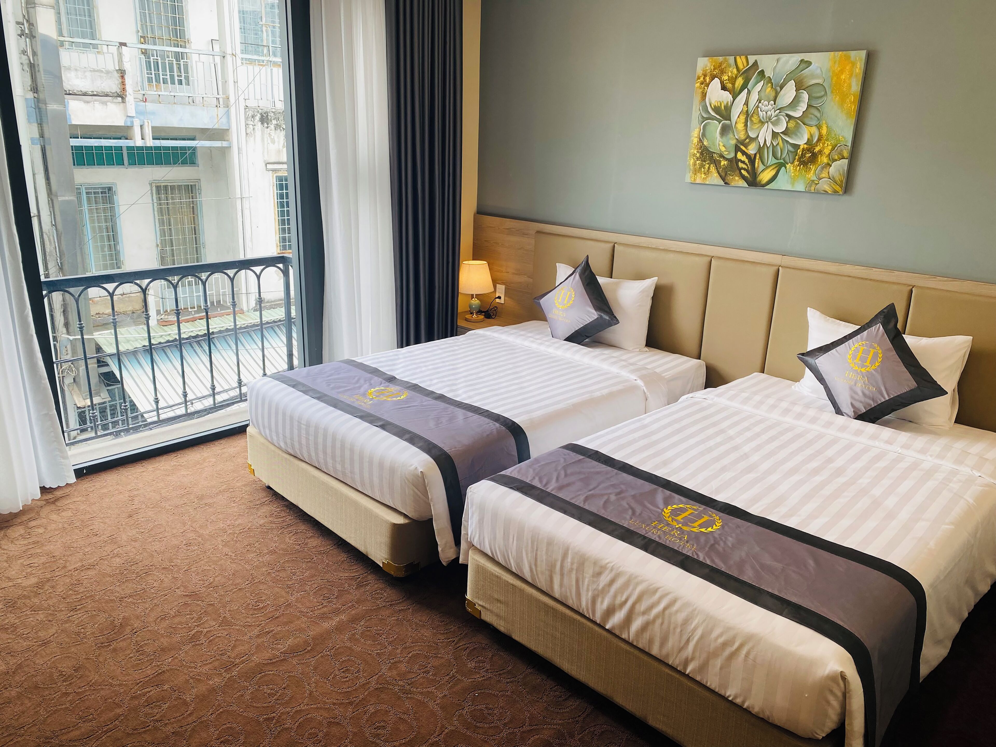 Une chambre d’hôtel avec deux lits, un balcon, un tableau et une vue sur les immeubles.