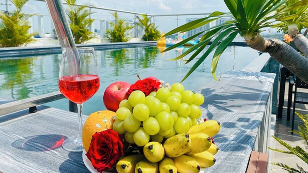 A table with a fruit platter, a glass of red wine, and a poolside view. - Hera Luxury Hotel (Ho Chi Minh City)