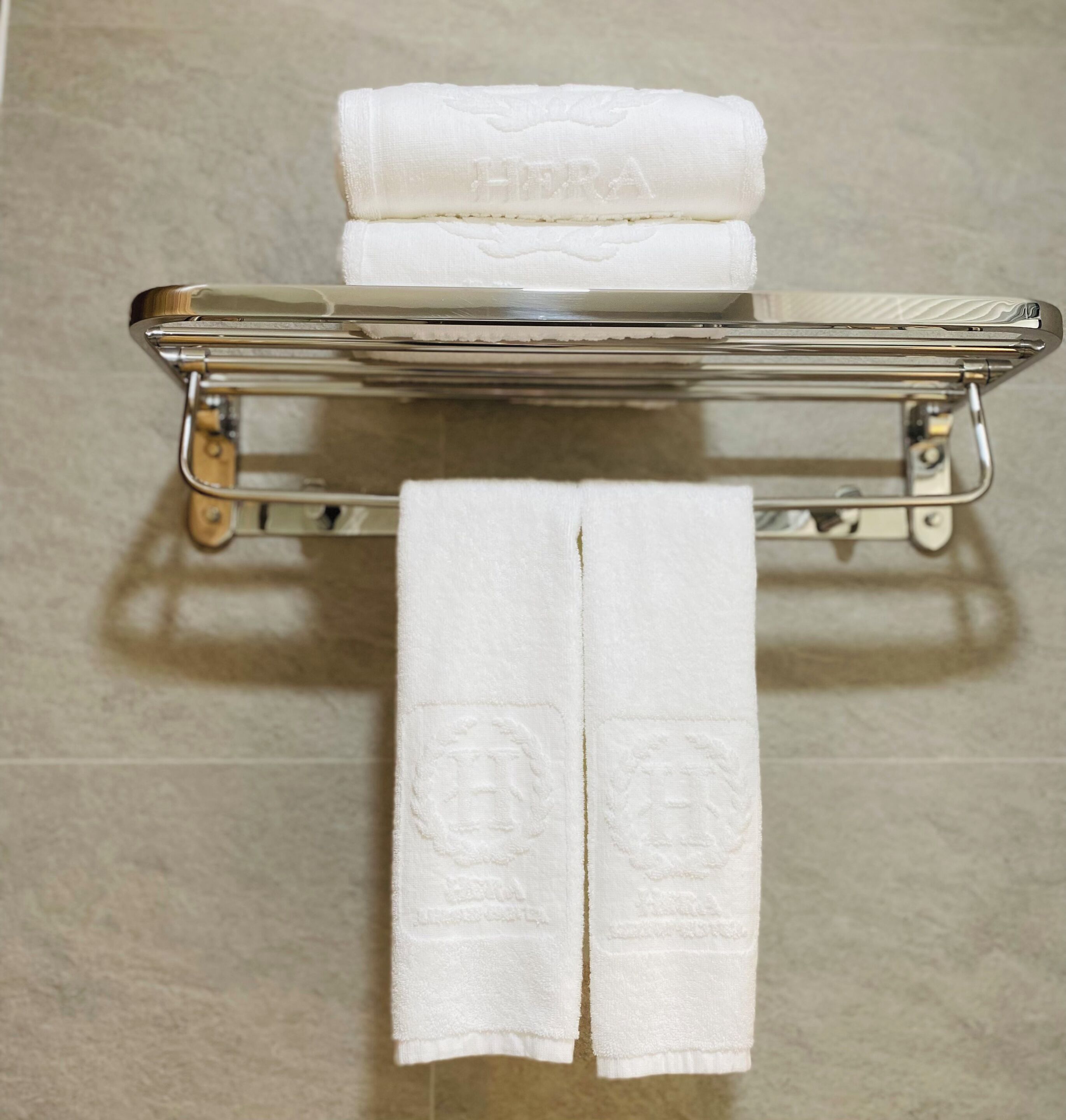 A bathroom with a metal towel rack holding two folded white towels and a rolled white towel.
