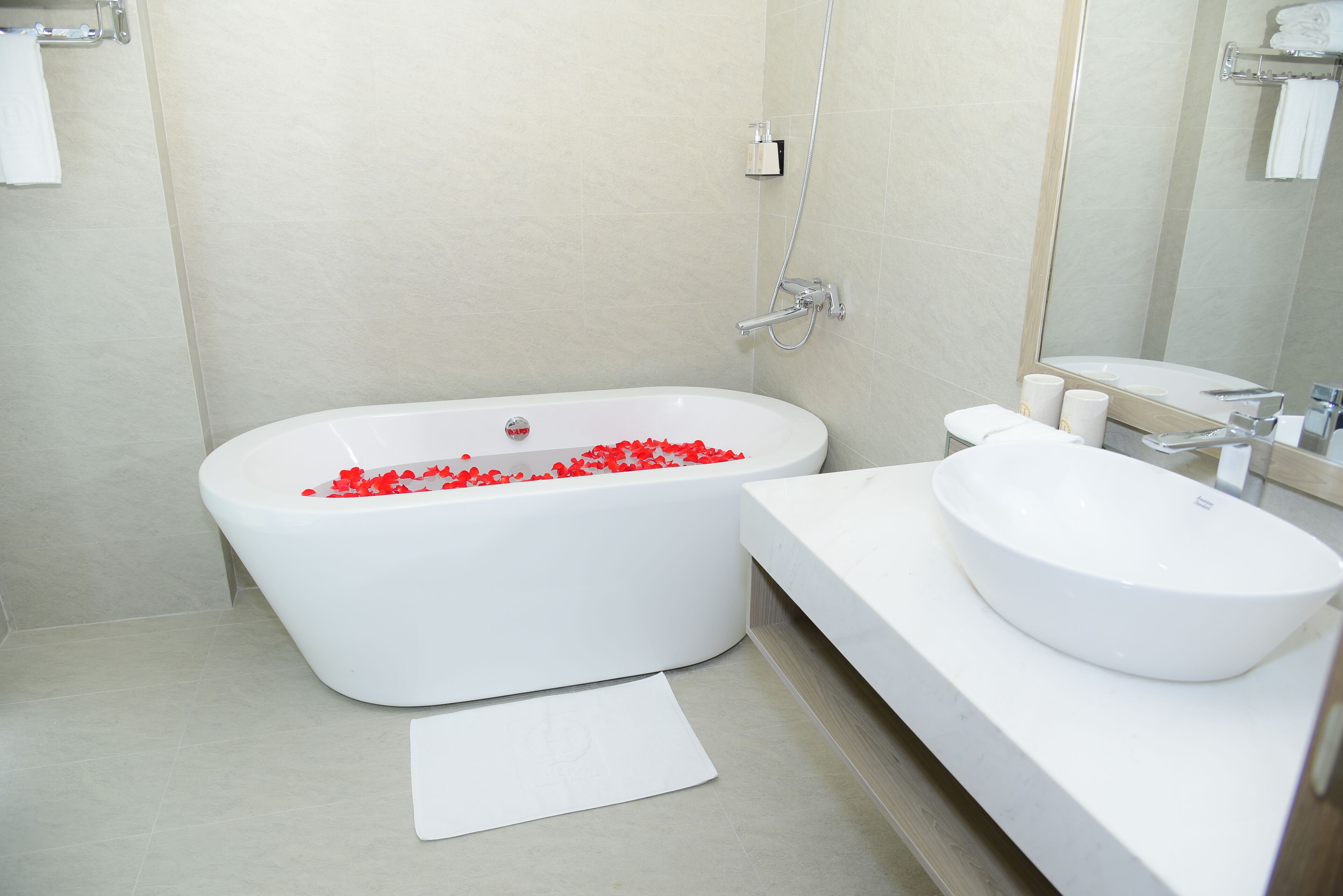 A modern bathroom with a freestanding bathtub filled with red bath products, a white sink, and a large mirror.